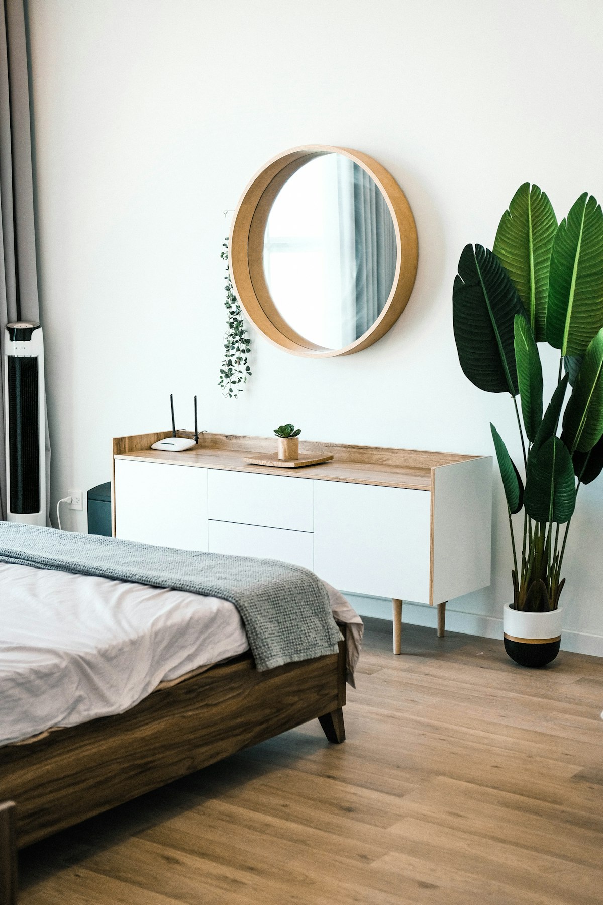 Quarto mobiliado com cômoda de madeira, espelho redondo e planta decorativa