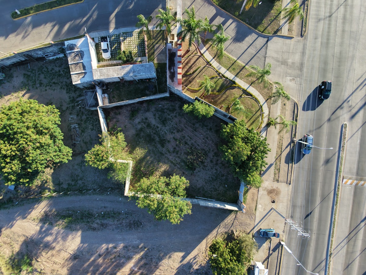 Vista aérea de terreno urbano vazio, cercado por árvores e via pública